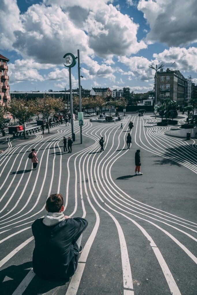 A person in a hoody sitting on a car-free, wavy square in Copenhagen