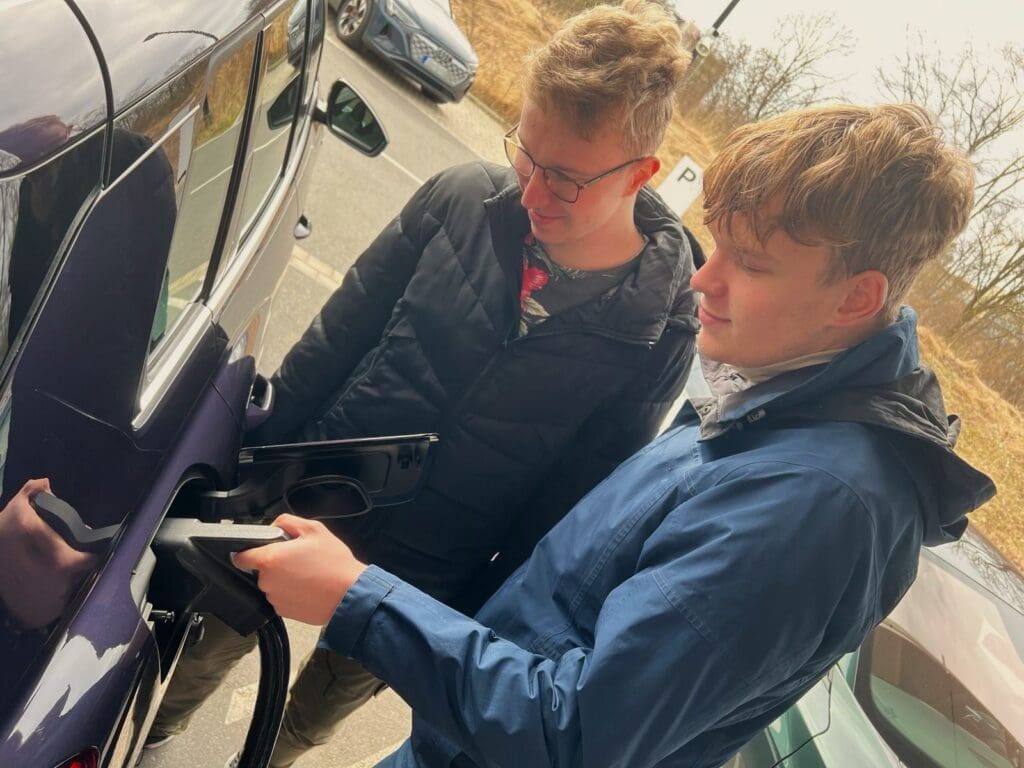 Two young men charging a modern full Electric Vehicle (EV) in a shiny purple color