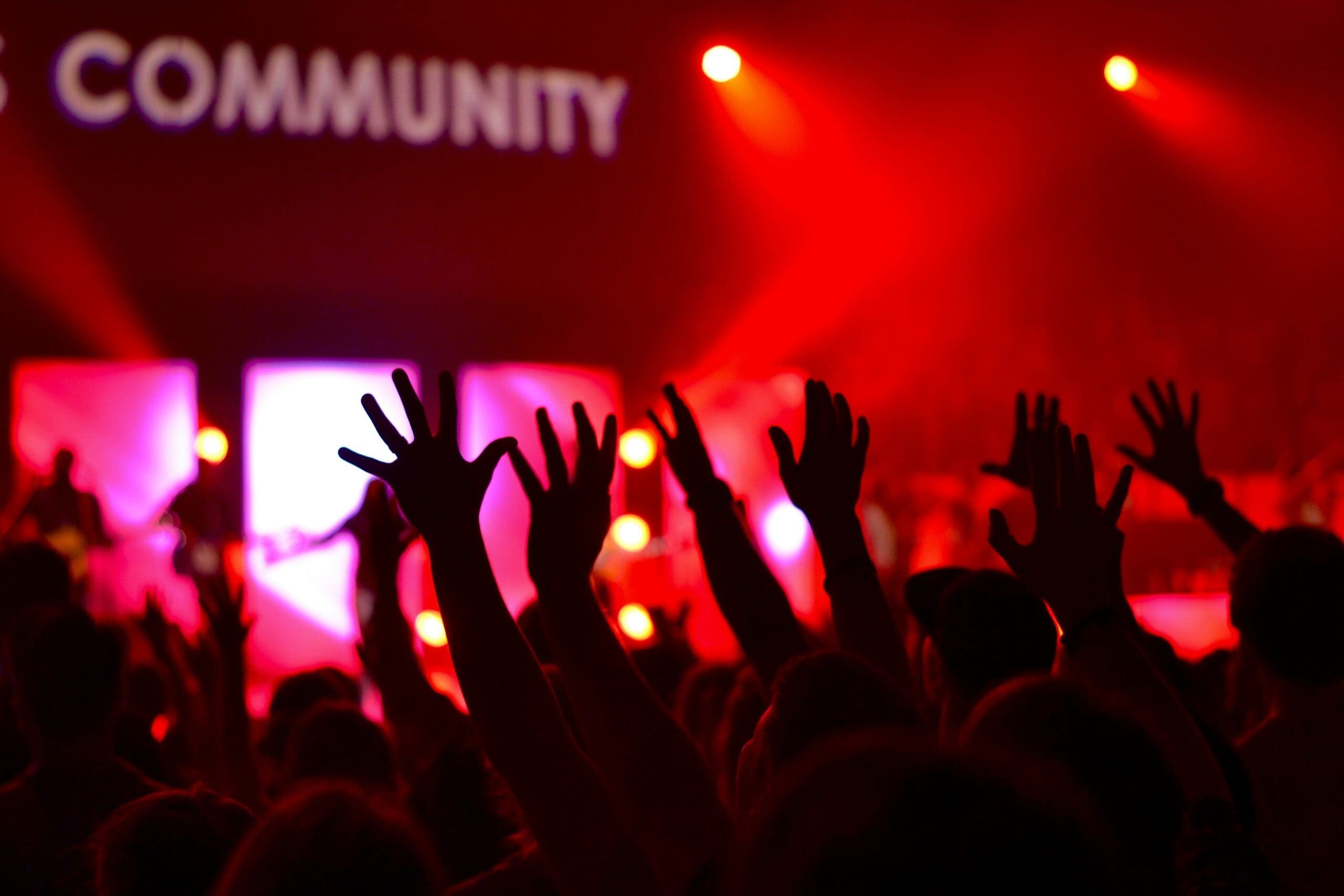 A crowd in front of a music stage, raising their hands, cheering the band and enjoying the moment