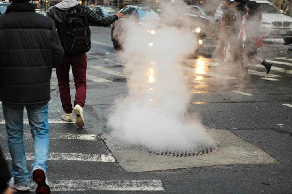 Die Hitze des Abwassers wird durch den Dampf sichtbar, der aus einem Gullyschacht an einer belebten Straßenkreuzung austritt