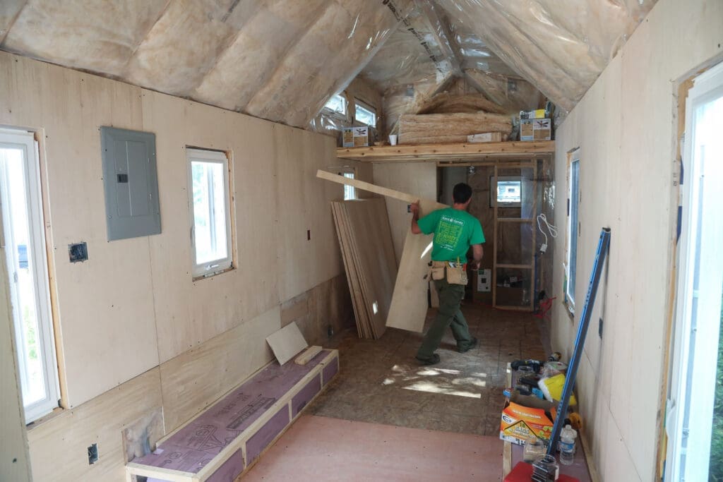 Inside, a view of a tiny house under construction reveals insulation layers visible beneath the roof. The small size of tiny houses and proper insulation allow them to consume significantly less energy compared to "standard" houses.