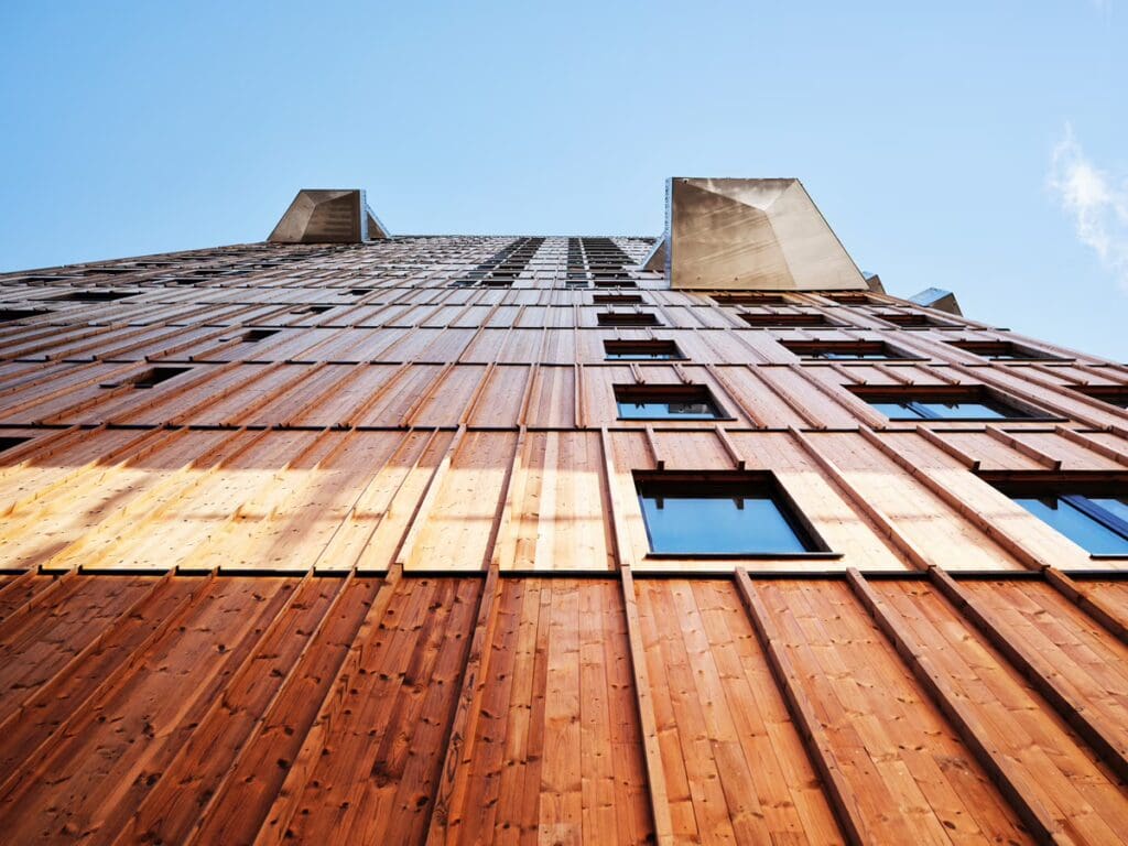 Looking up at one of the Vertikal Nydalen towers with its wooden façade and two balconies jutting out against the sky