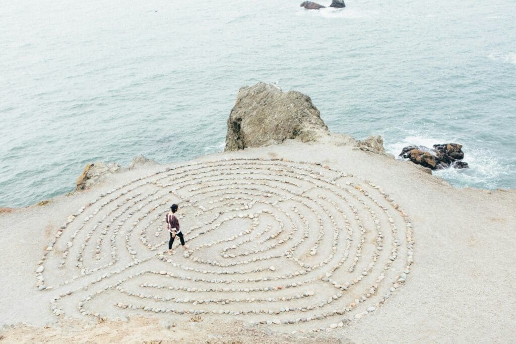 Eine Person, die in einem Labyrinth aus flachen Steinen auf einem Strand spazieren geht.