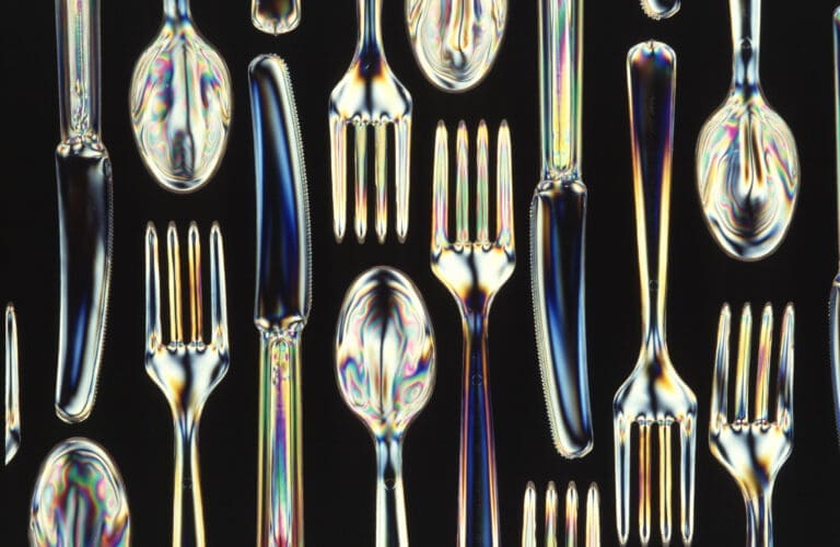 Glistening and transparent biodegradable plastic knives, forks and spoons laid on a black surface