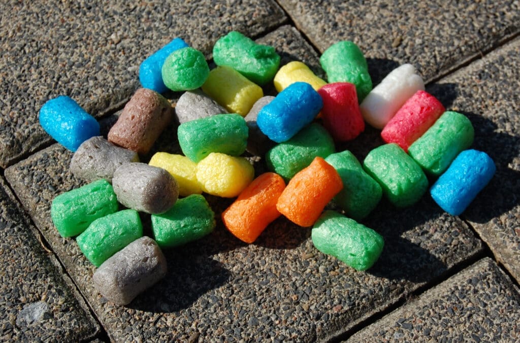 Bunte Schaumstoffstücke aus Maisstärke liegen auf einem grauen Pflaster