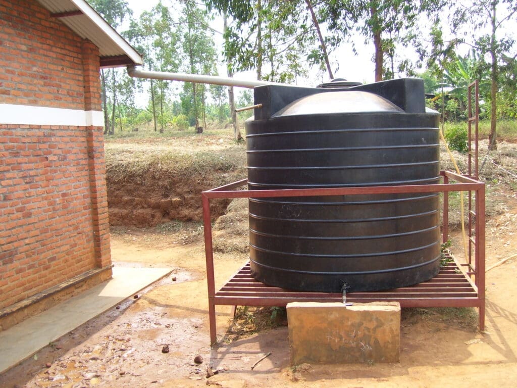 Big plastic rainwater tank connected to the roof of a small brick house