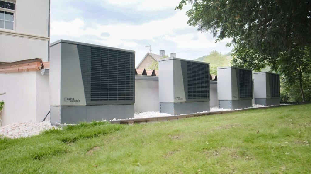 Array of four heat pump boxes along a residential lawn