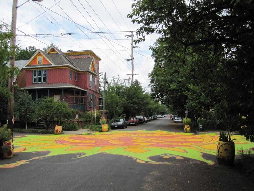 Colorful sunflower mural painted across a residential intersection in Portland's Sunnyside neighborhood, part of City Repair's intersection repair program reclaiming streets as community spaces